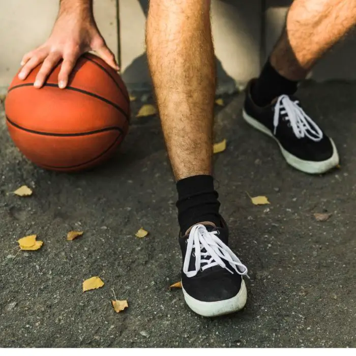 Man dribbling a basketball on an outdoor court wearing black athletic basket ball shoes with white laces.